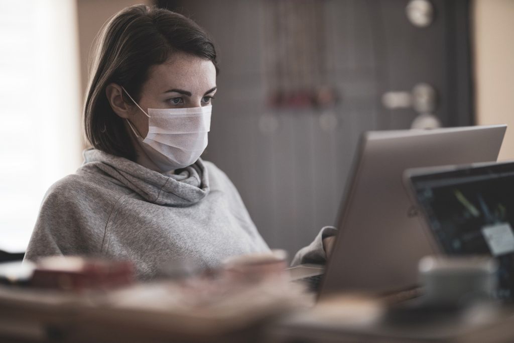 Eine junge Frau mit einer Maske arbeitet an einem Computer.
